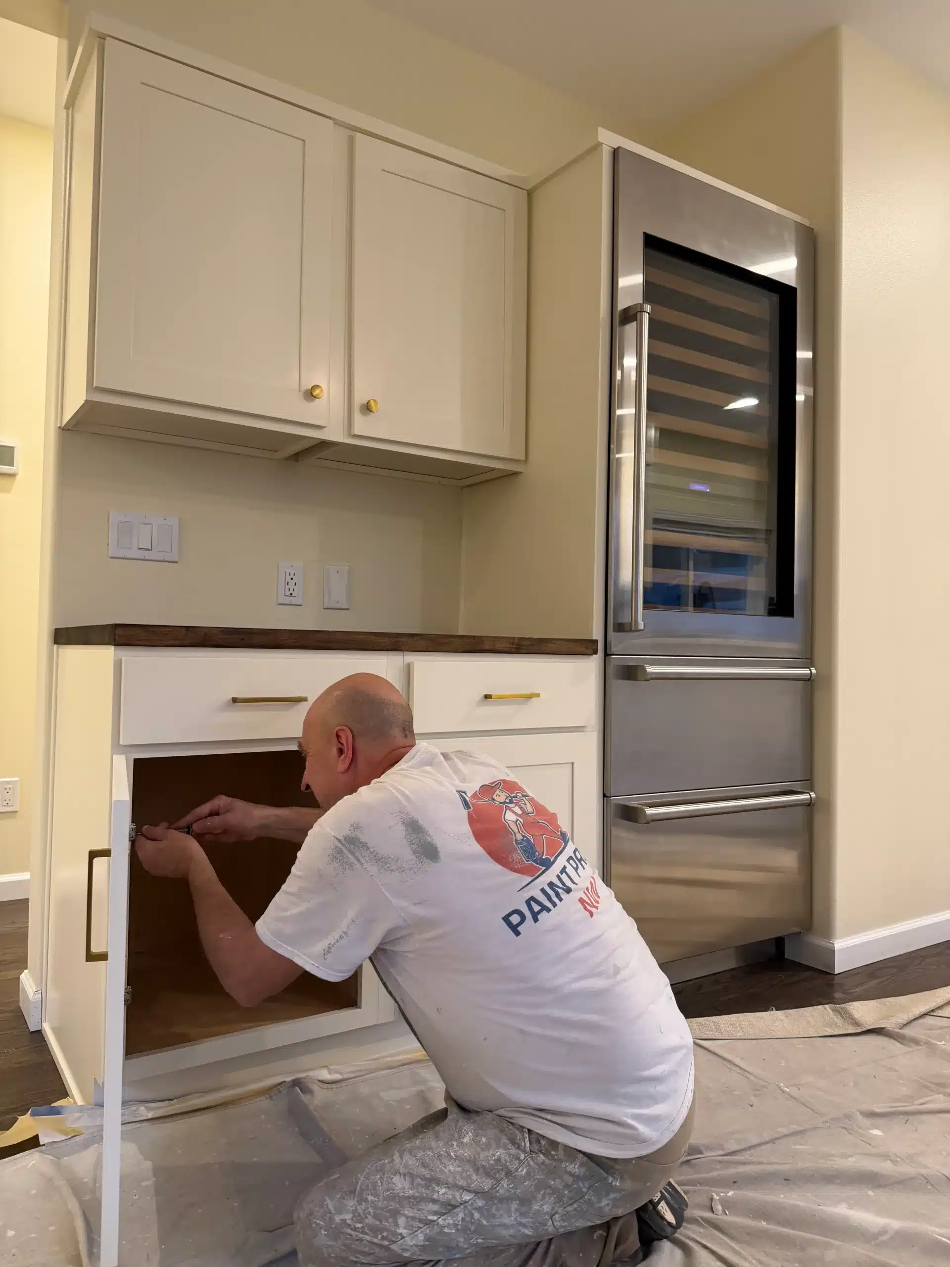 Professional Painter Installing Kitchen Cabinet Hardware A professional painter installing hardware on newly painted white kitchen cabinets next to a wine refrigerator.