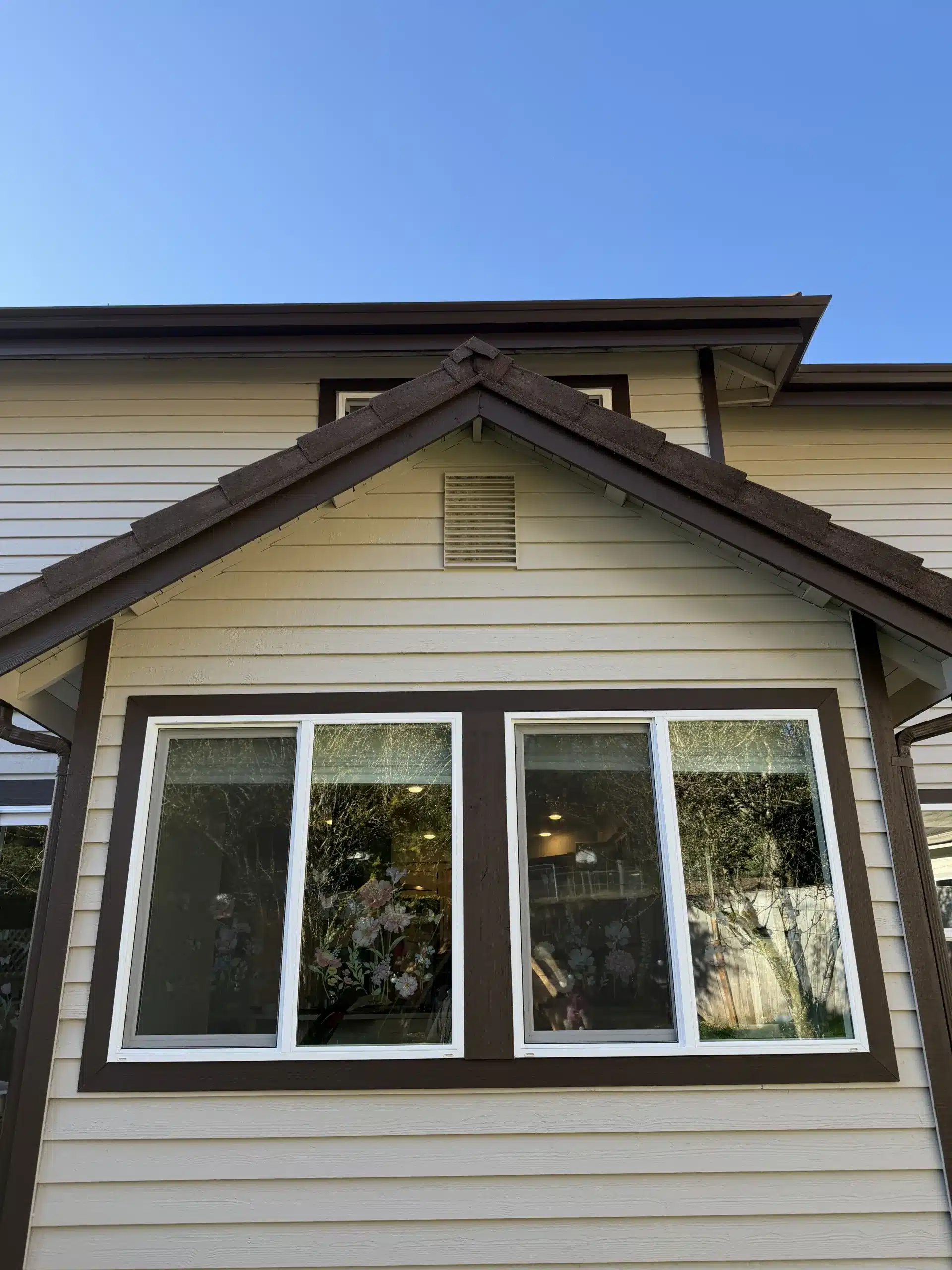 Residential Exterior Painting with Beige Siding and Brown Trim Upper exterior of a residential house featuring light beige siding and contrasting dark brown window and roof trim.