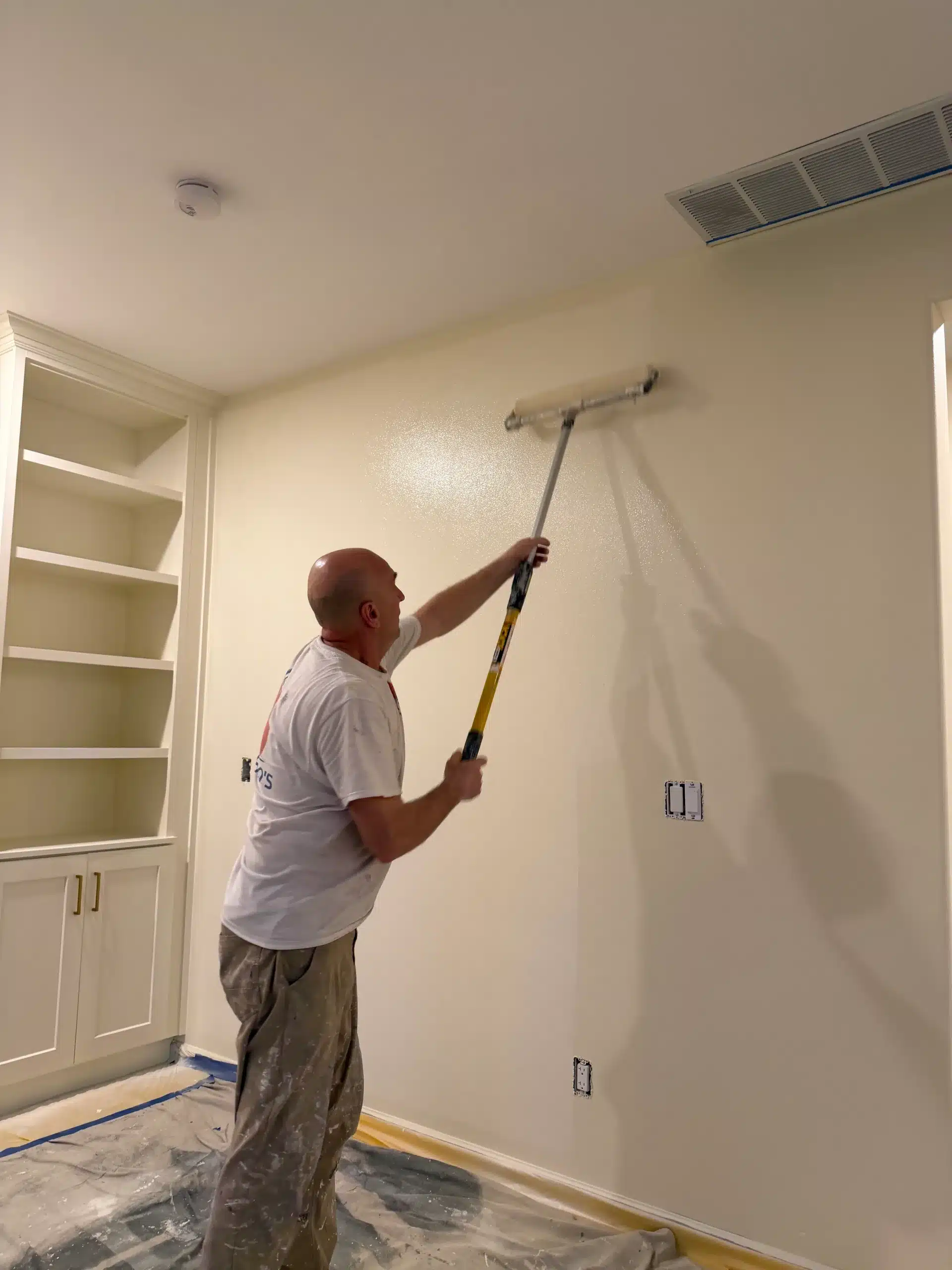 Professional Painter Applying Interior Wall Paint A professional painter using a roller on an extension pole to paint an interior room wall light beige.