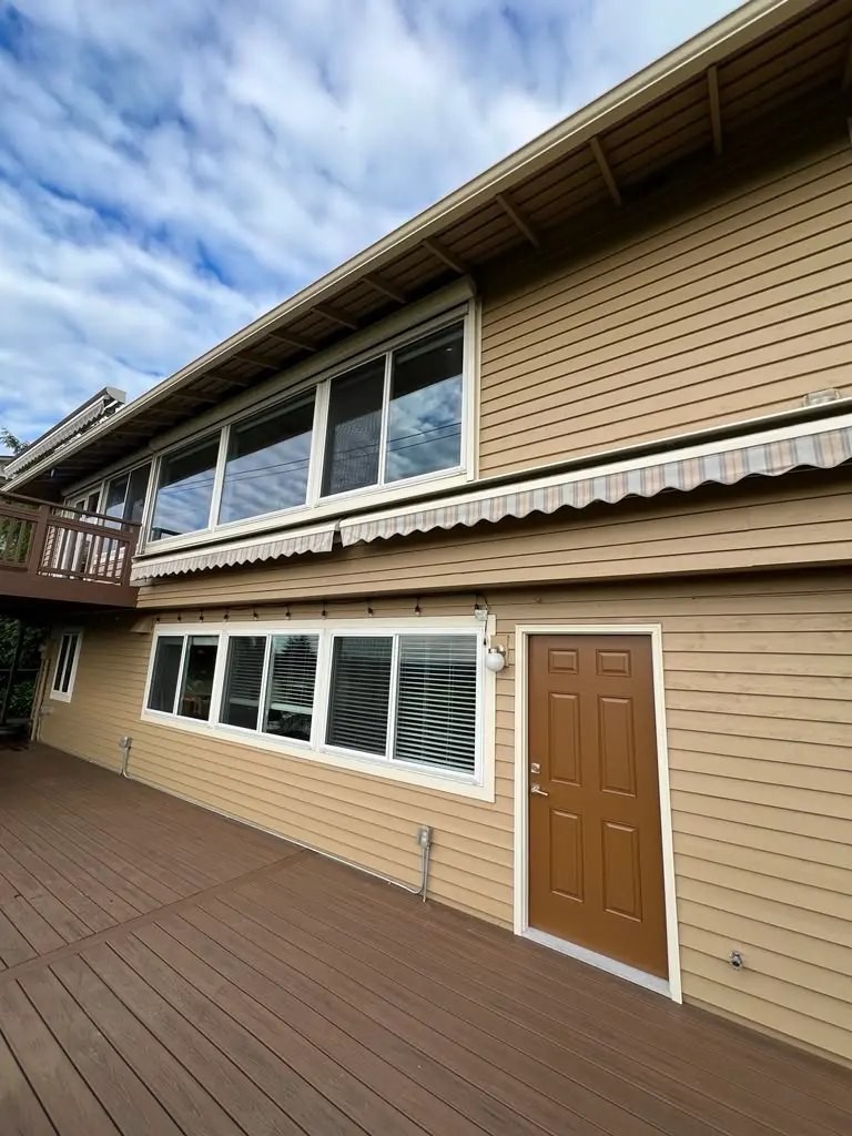 Residential Exterior Painting for Homes with Siding and Decks Home exterior with light brown siding, white trim, a brown door, and a large wooden deck.